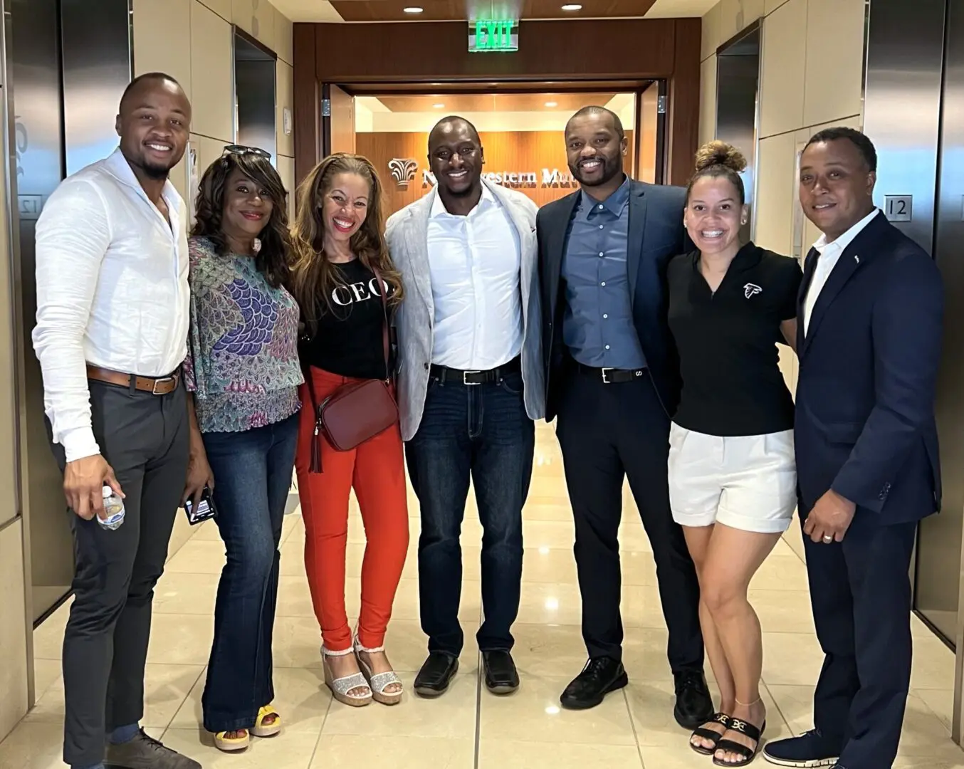 Group of seven people smiling in hallway.