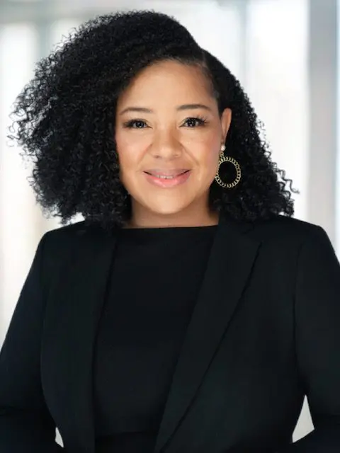 Smiling person in black blazer, curly hair.