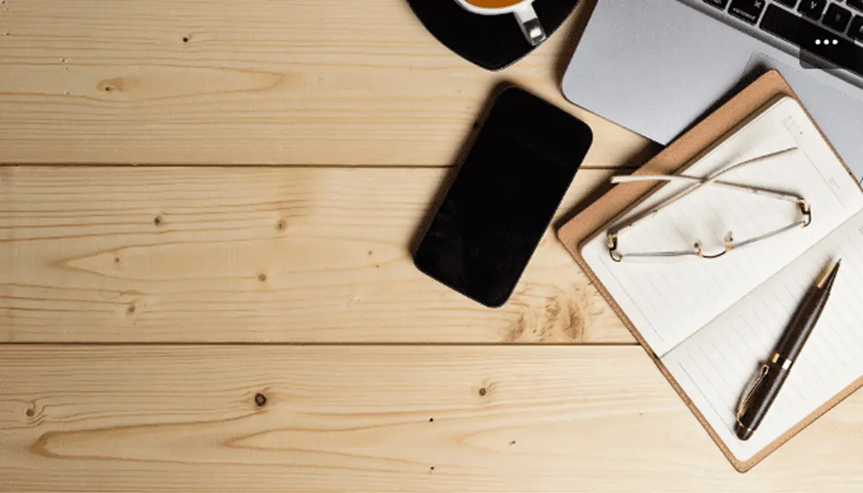 Wooden desk with phone, laptop, notebook, glasses